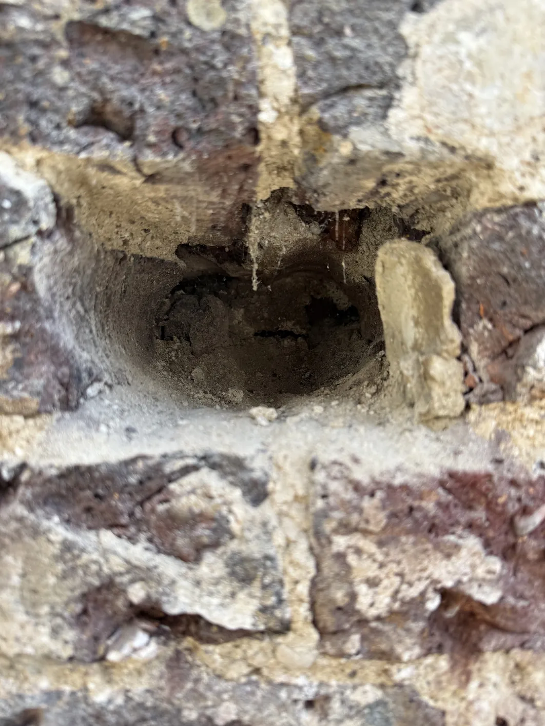 A close-up of a mortar joint between bricks showing dark deterioration and spalling damage, with light-colored cement deposits visible