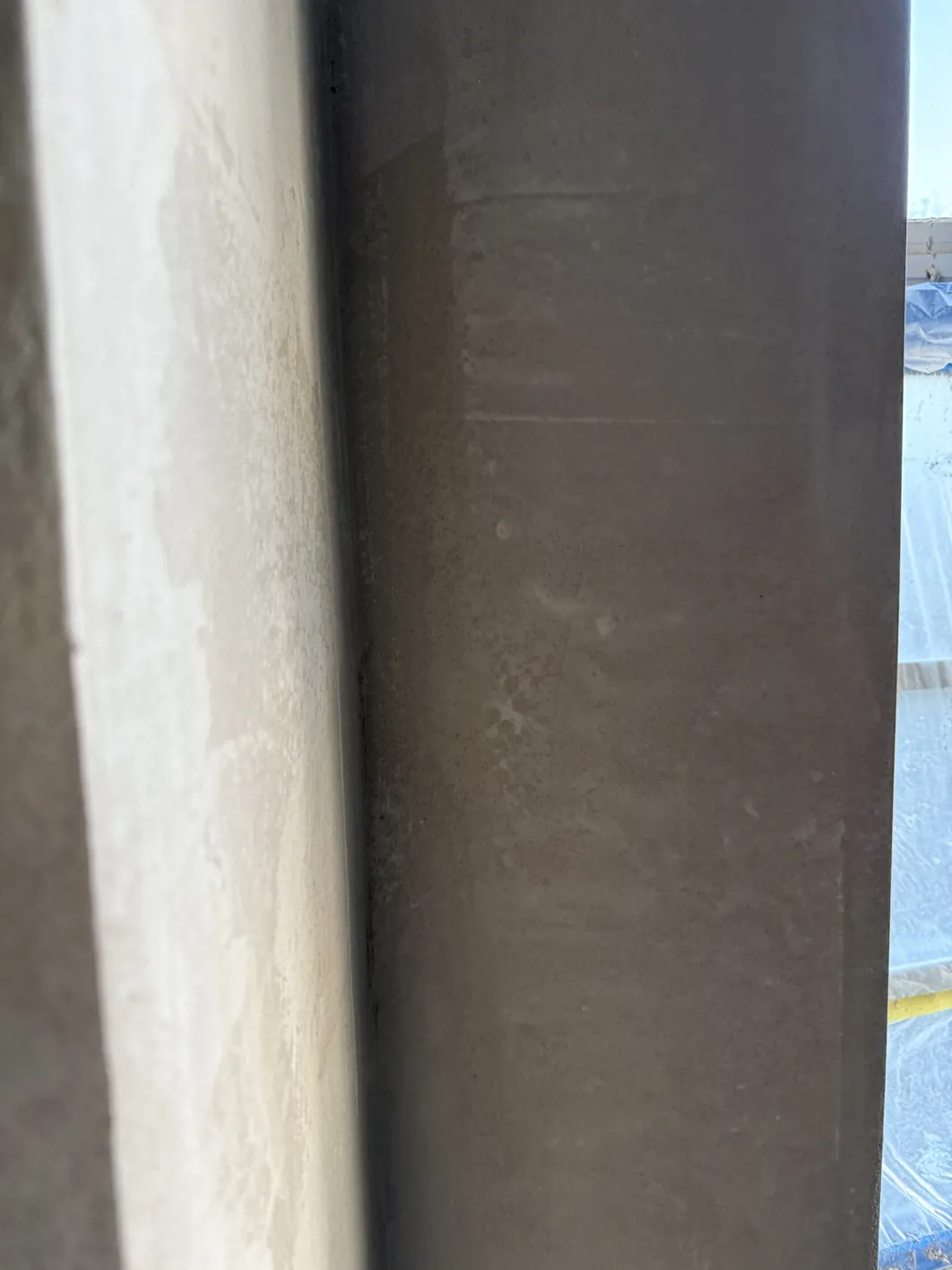Two vertical wall surfaces meet at an edge: a light cream-coloured lime plaster finish on the left and a darker grey surface on the right.