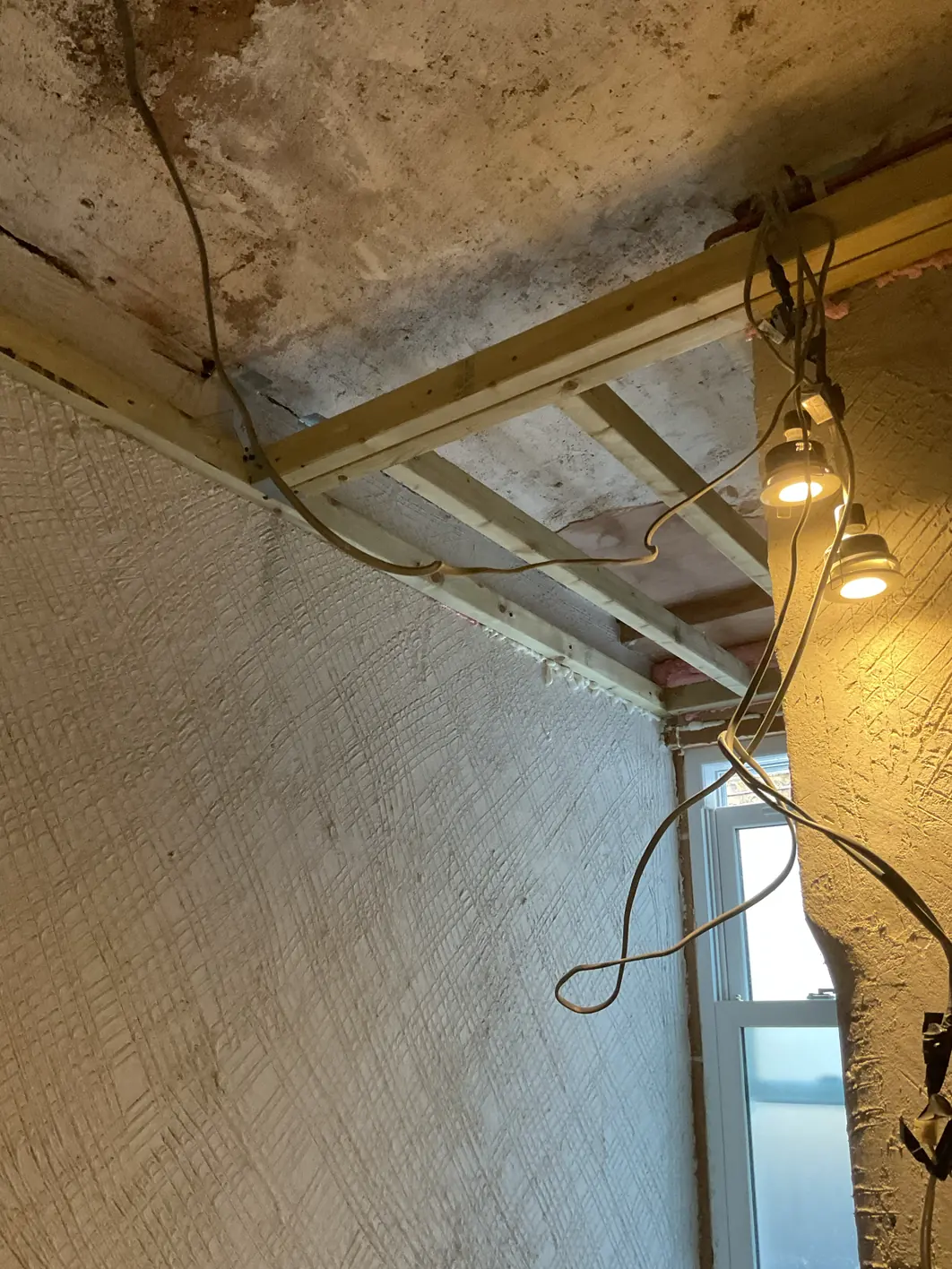Wall covered in a base coat scored all over with a close cross-hatch pattern, below a ceiling stripped back to bare joists