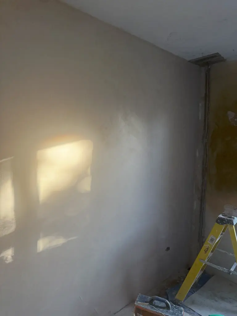 Large finished wall lit from the side, the raking light showing an even surface with no hollows or ridges, coarser base coat visible on the return