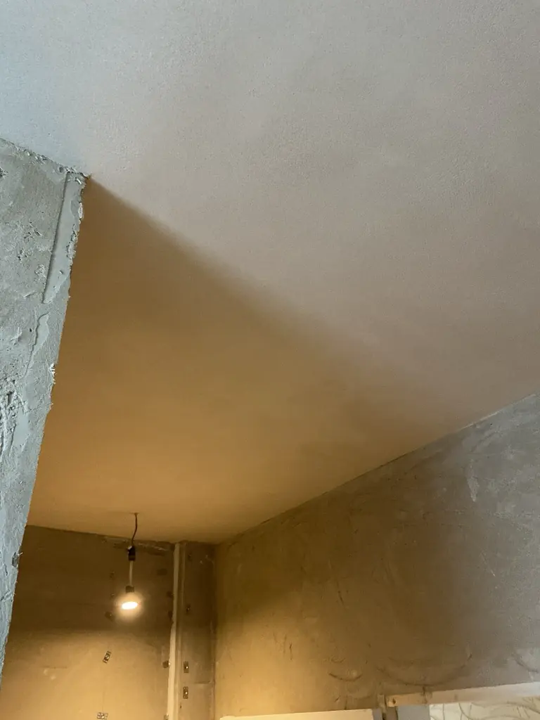 Ceiling finished in a smooth pale top coat, meeting walls still in their coarser base coat
