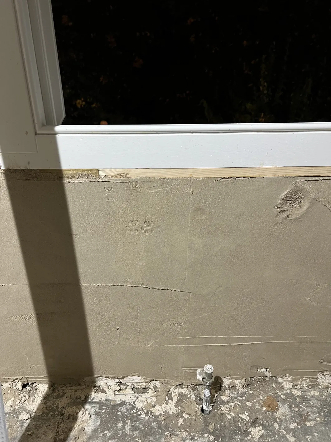 Pale lime plaster on wall showing fine shrinkage cracks, with white painted window reveal above and concrete plinth below