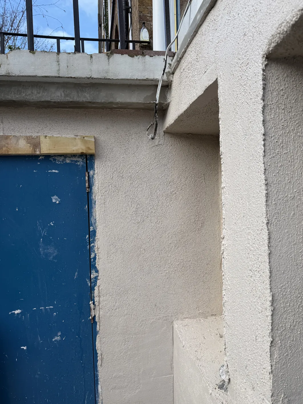 Newly rendered stone masonry wall with window reveal, featuring textured finish coat over preparatory base coats