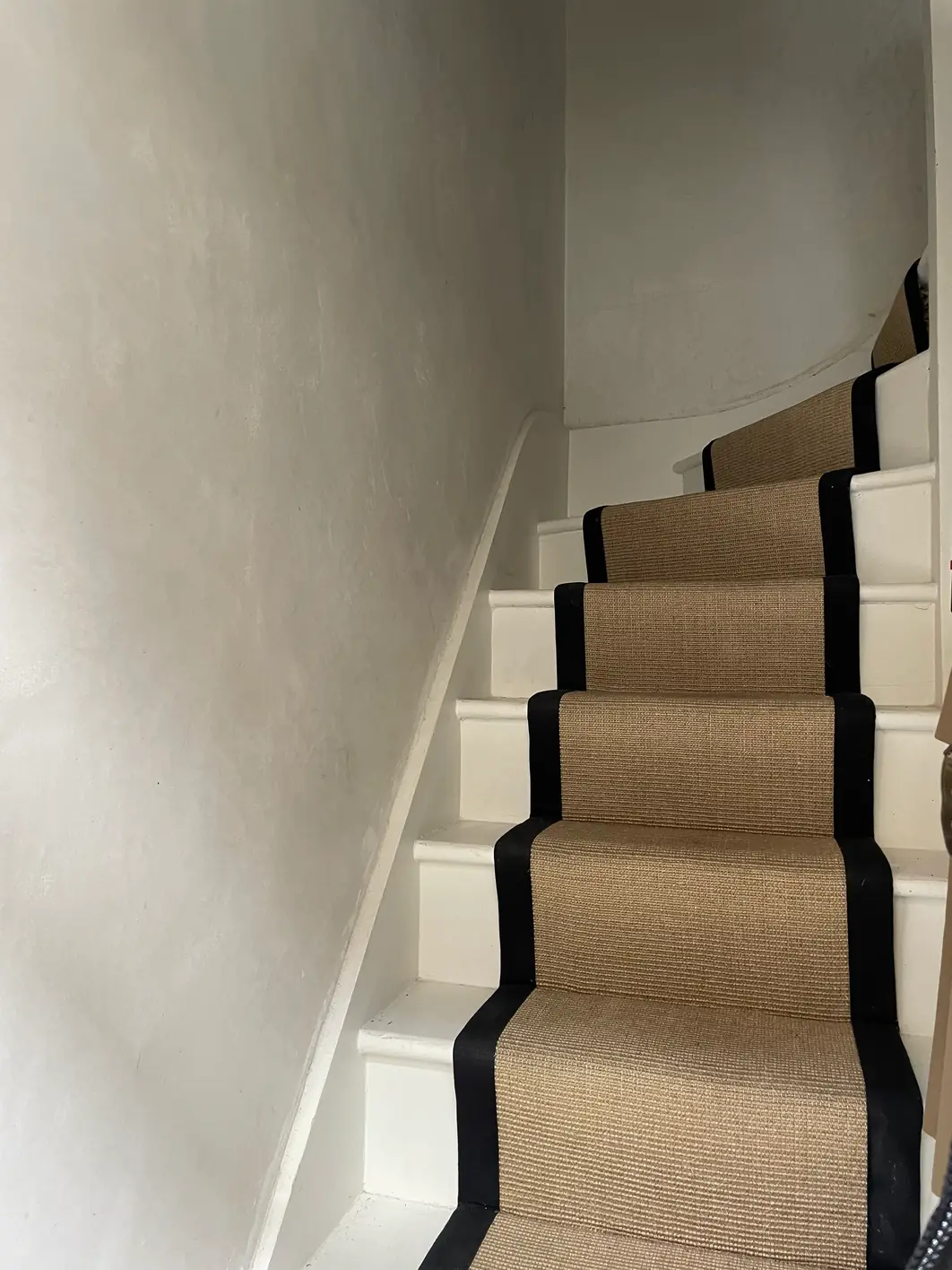 Curved stair wall finished in one continuous run of smooth lime plaster, beside white painted stairs fitted with a sisal runner