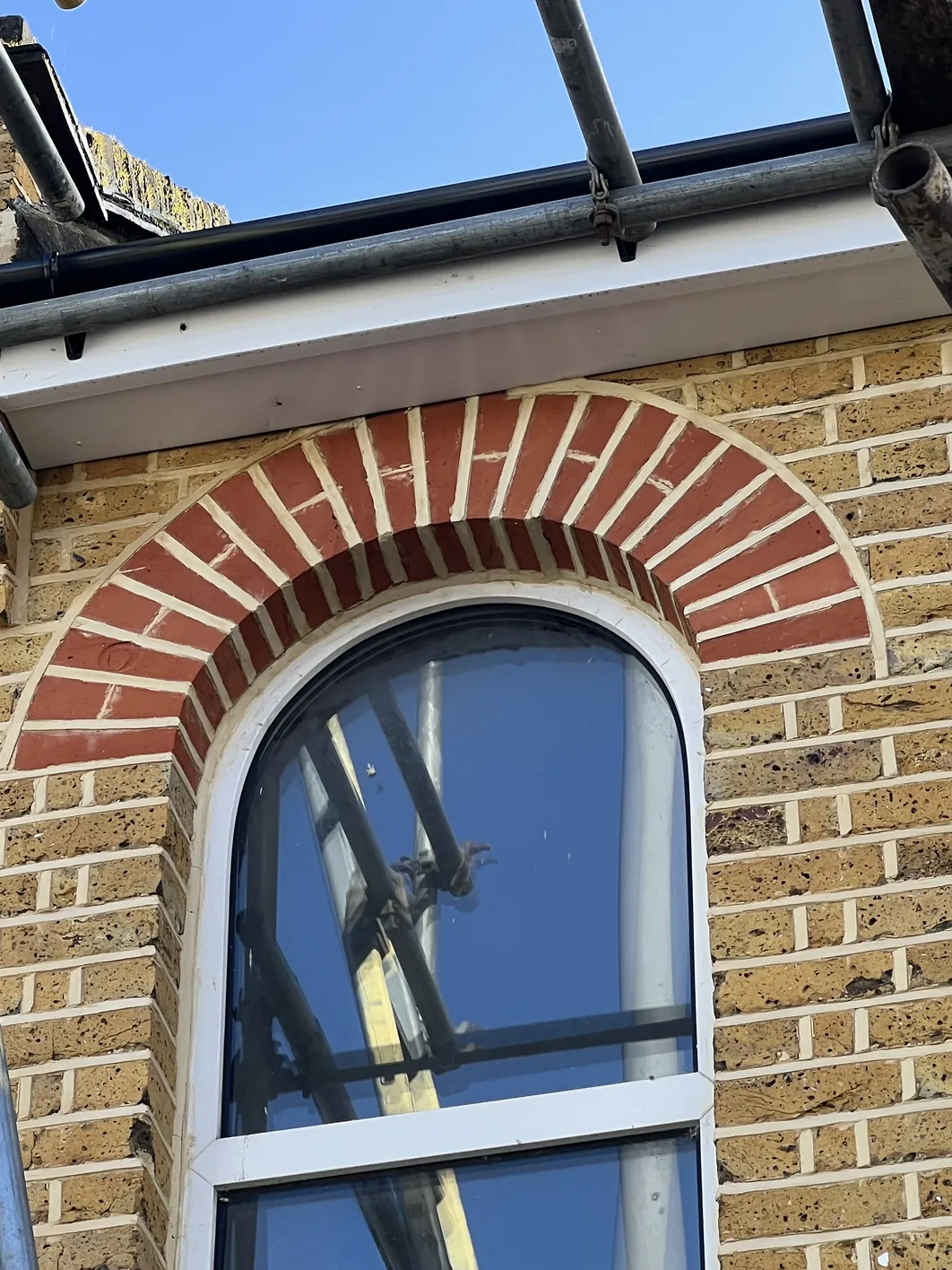 Rounded arch window with red brick voussoir detail, white frame, set in light tan brick wall with cream mortar joints