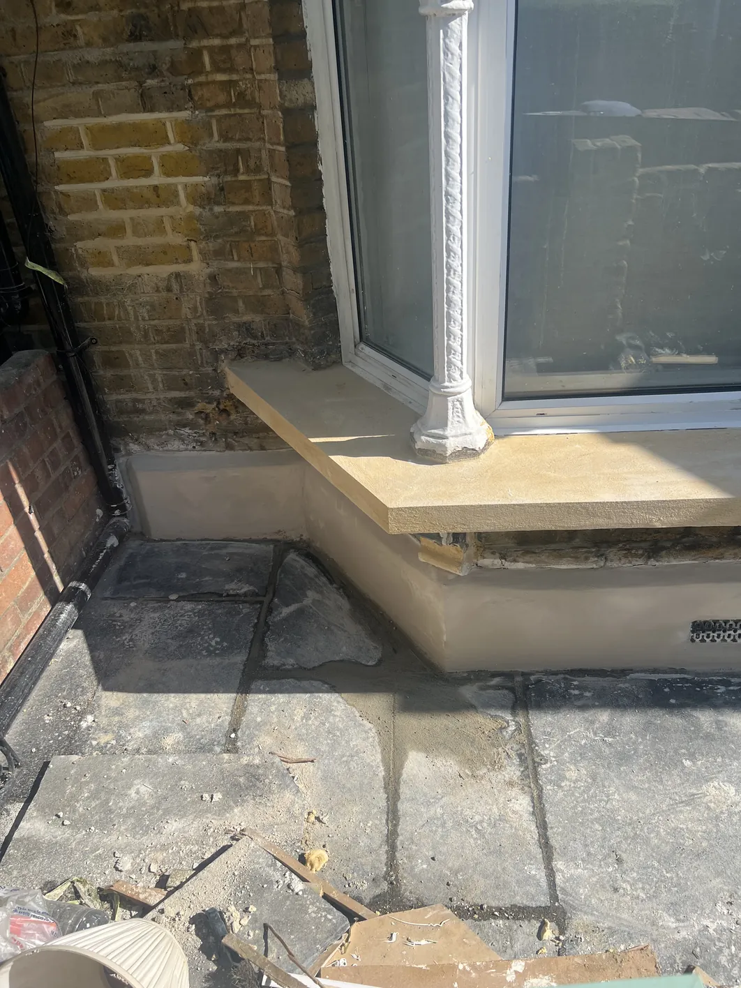 Cream-coloured render coat applied around a white-framed window opening in a brick chimney breast, with a window sill and reveal under preparation