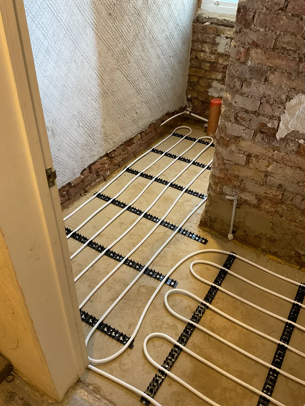 Underfloor heating pipe clipped into track laid across the cured limecrete slab, run in loops ready to be encased.