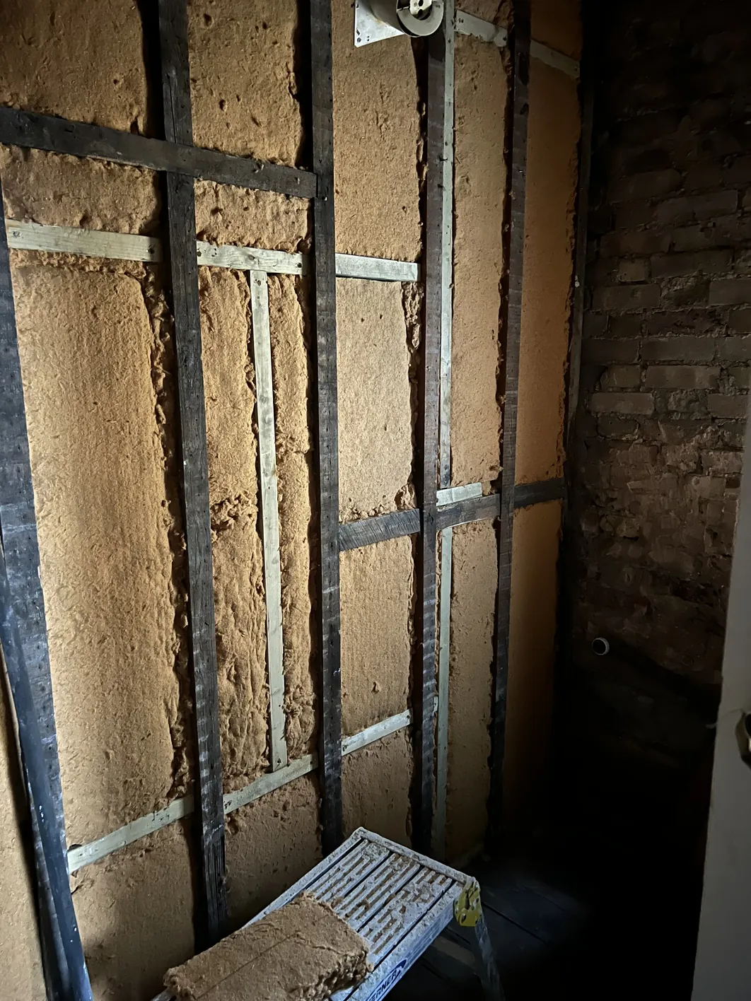 Cork-coloured insulation batts fitted vertically between dark timber studs, held with metal straps at intervals